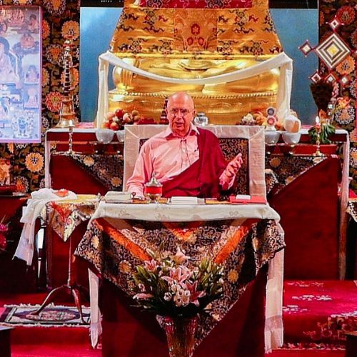 Denys Rinpoché donnant la Transmission Fondamentale Ekāyāna depuis son siège d'enseignement, devant un autel bouddhiste orné de thankas et d'une grande statue dorée — Nigu Karma Ling, Arvillard, Savoie